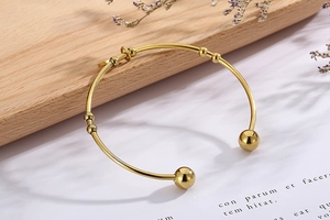 Detailed side view of a gold-tone stainless steel open bangle with beads and ring accents