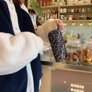 Close-up of floral corduroy pencil case with zipper and tag in a cozy cafe setting