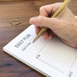 Close-up of hand writing on daily planner pad with a premium gold pen on wooden desk