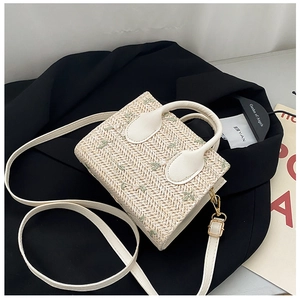 Detail of floral embroidery on a cream straw tote bag with leather strap and top handle
