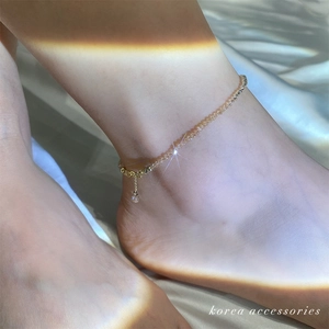 Close-up of beaded anklet with crystal teardrop charm on model wearing light silk fabric