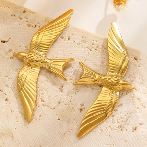Detail of golden swallow bird stud earrings with feather texture on stone tray