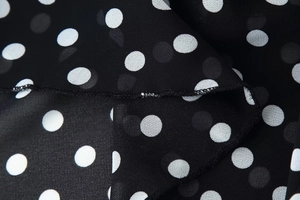 Macro shot of white polka dot print on black chiffon fabric with neat hem stitching
