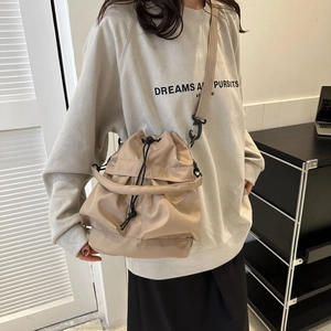 Vue détaillée du sac seau beige en nylon avec cordon et bandoulière noire sur modèle