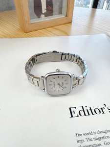 Macro view of silver square quartz watch with white dial on editor's paper background