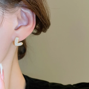 Détail de la boucle d'oreille en forme de L dorée avec zircons sur le mannequin