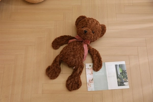 Detail of plush brown teddy bear with red plaid bow on rustic light wood floor