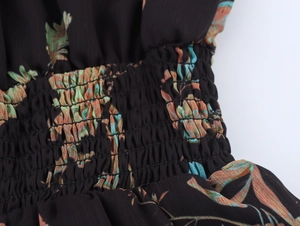 Detailansicht der gesmokten Taille eines schwarzen Chiffonkleides mit floralem Blattmuster