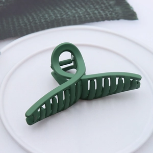 Detail of dark green matte hair claw clip on white tray showing anti-slip teeth and texture