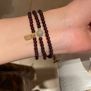 Detail of garnet beaded bracelet with a gold Fu pendant on woman's wrist