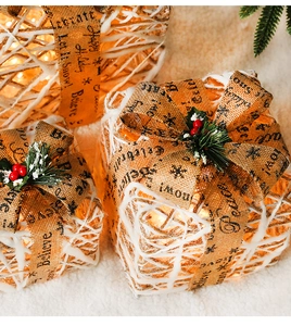 Close-up of lighted rattan Christmas gift boxes with pine cones and burlap ribbons