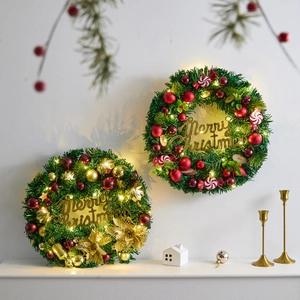 Christmas pine needle wreath with gold stars, red balls and warm LED lights on a white mantel