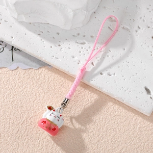 Detail of white Lucky Cat charm with red accents and pink strap on textured stone
