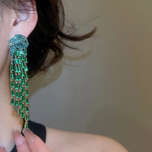 Détail de boucles d'oreilles pompons avec zircons verts et chaînes dorées sur modèle
