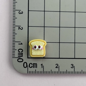 Detailed size view of yellow resin toast charm with big eyes on a centimeter scale mat