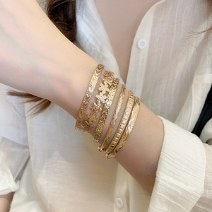 Gros plan d'un ensemble de six bracelets dorés avec motifs fleurs et étoiles au poignet