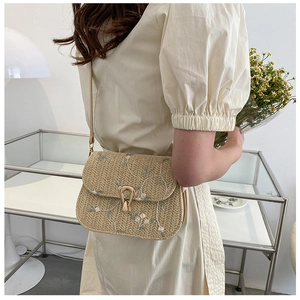 Detail of beige straw crossbody bag with pink floral embroidery and vintage gold lock
