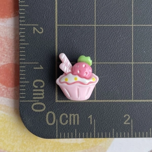 Close-up of a 1.5x1.8cm pink resin strawberry cupcake charm on a black cutting mat