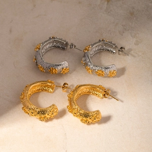 Detailed macro view of C-shaped stainless steel earrings with floral relief and textured finish