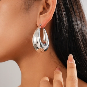 Close-up of a silver-toned hollow teardrop earring worn on ear for fashion display