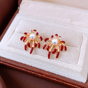 Close-up of gold-plated firework earrings with white pearls and red enamel details