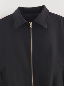 Detaillierte Nahaufnahme einer schwarzen Jacke mit Reverskragen und goldener Reißverschluss