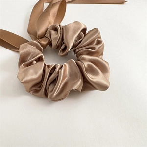 Detailed texture of champagne gold satin scrunchie with long ribbons on white surface