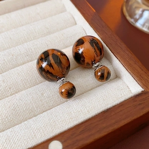 Detail of leopard print double-sided resin stud earrings on a beige velvet jewelry tray
