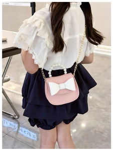 Detail of pink child crossbody bag featuring large white bow and elegant pearl handle