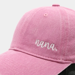 Detailed close-up of white 'nana' script embroidery on pink washed cotton baseball cap