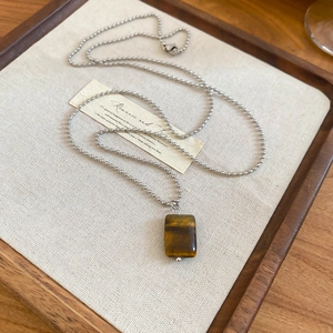 Detail of tiger eye stone pendant with silver bead chain on vintage wooden tray