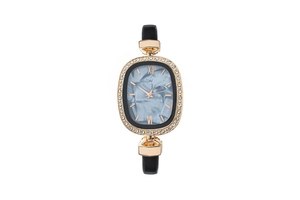 Detail of oval gold watch with marble dial and rhinestone bezel on black leather strap
