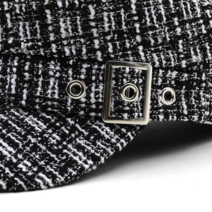Detail of black and white tweed newsboy hat with silver metal buckle and eyelets