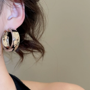 Close-up of a polished silver-finish wide hoop earring worn on a female model's ear