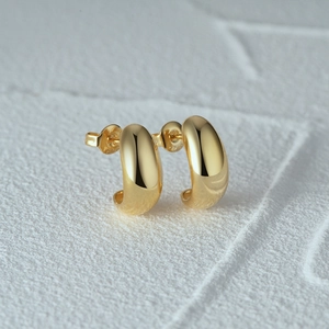 Close-up of polished gold C-shape stud earrings with S925 hallmark on a stone base