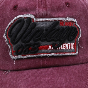 Close-up of vintage 3D embroidery and distressed fabric detail on a burgundy baseball cap