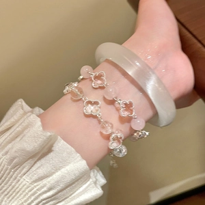 Close-up of stacked lucky clover charm bracelets and a translucent white bangle on wrist