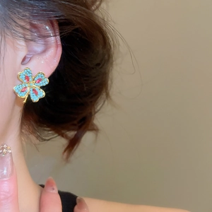 Macro detail of gold clover earring with blue beads and a red center gemstone