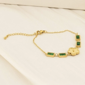 Detail of gold chain bracelet featuring green rectangular gemstones and sunflower pendant