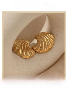 Macro detail of golden shell stud earrings with polished wave texture in French retro style
