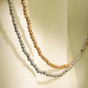 Nahaufnahme minimalistischer Perlenketten in Gold und Silber mit polierter Metallstruktur