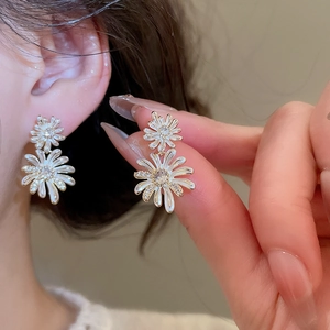 Macro shot of double-layer daisy drop earrings featuring white enamel and zircon accents
