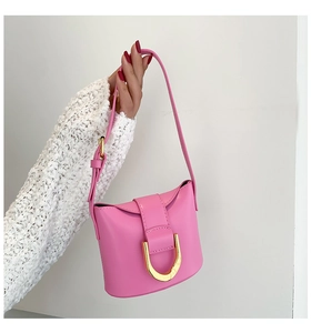 Detail of pink leather handbag with gold D-ring buckle held by a model in white knitwear