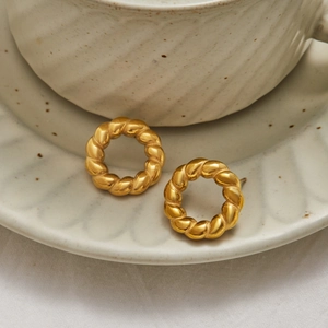Detailed view of golden woven texture round stud earrings on a ceramic dish