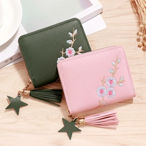 Floral embroidered leather zip wallets in pink and green with tassels on wood background