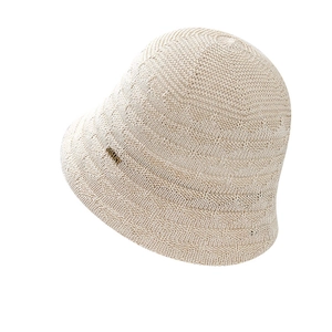 Beige hollow knit bucket hat for women with a minimalist metallic brand label detail