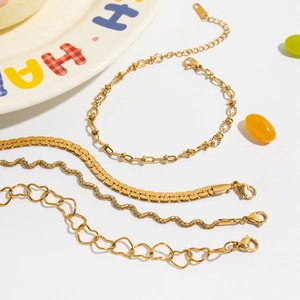 Flat lay of four gold stainless steel bracelets with heart clasp and snake chain designs