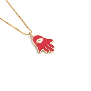 Detailed close-up of a golden Hamsa hand pendant with red enamel and a sparkling zircon eye