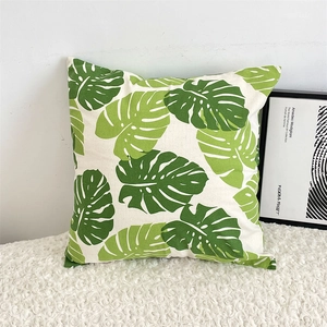 Detailed close-up of a green monstera leaf cotton linen pillowcase on a soft white sofa