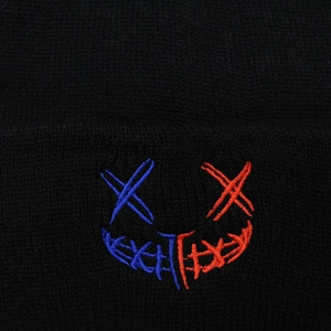 Dettaglio macro del ricamo smiley XX su un berretto in maglia nera a coste